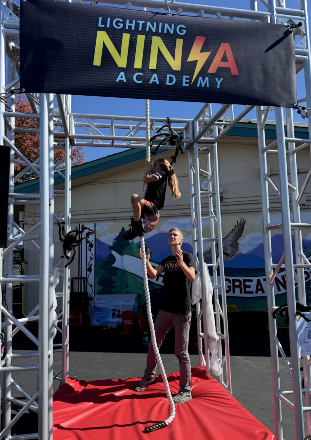A young ninja climbing the rope under the Lightning Ninja Academy banner